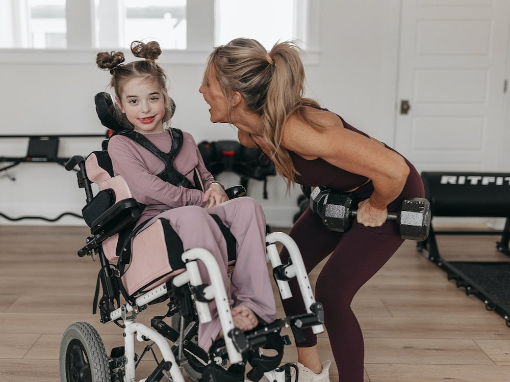 Shannon lifting weights and her daughter in a wheelchair next to her